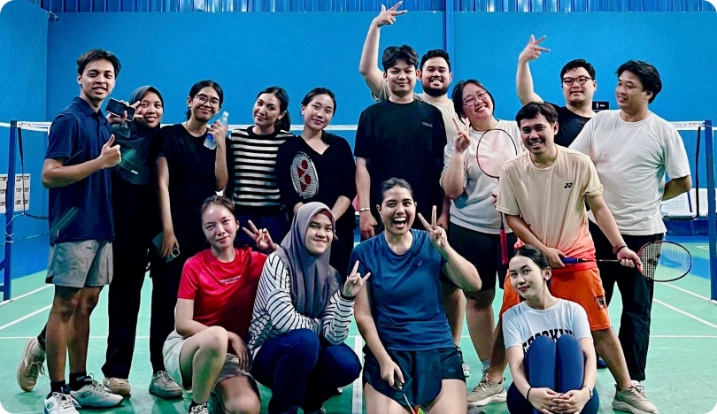 Group of eleven smiling people posing on an indoor pickleball court holding paddles and balls.